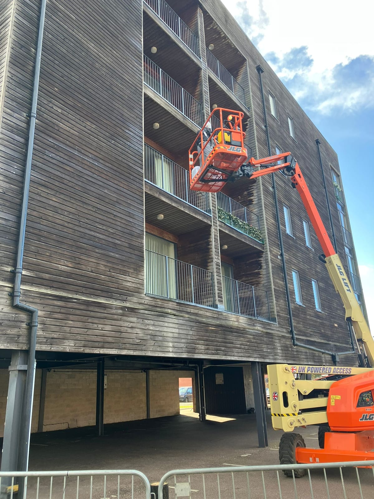 Technician treating external timber cladding from a mobile elevating work platform