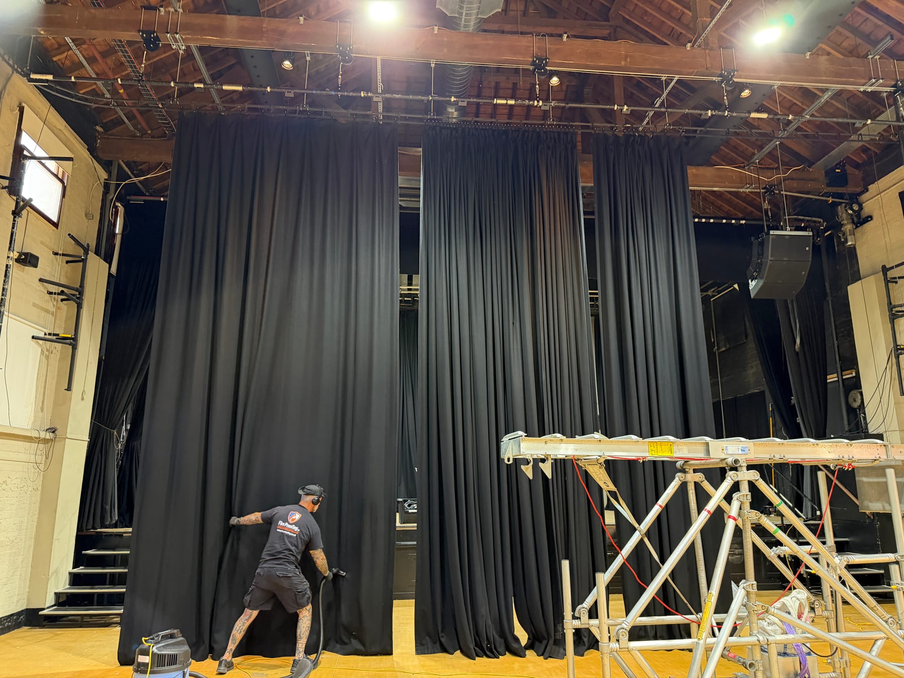 Technician professionally cleaning large black stage curtains while they remain hanging