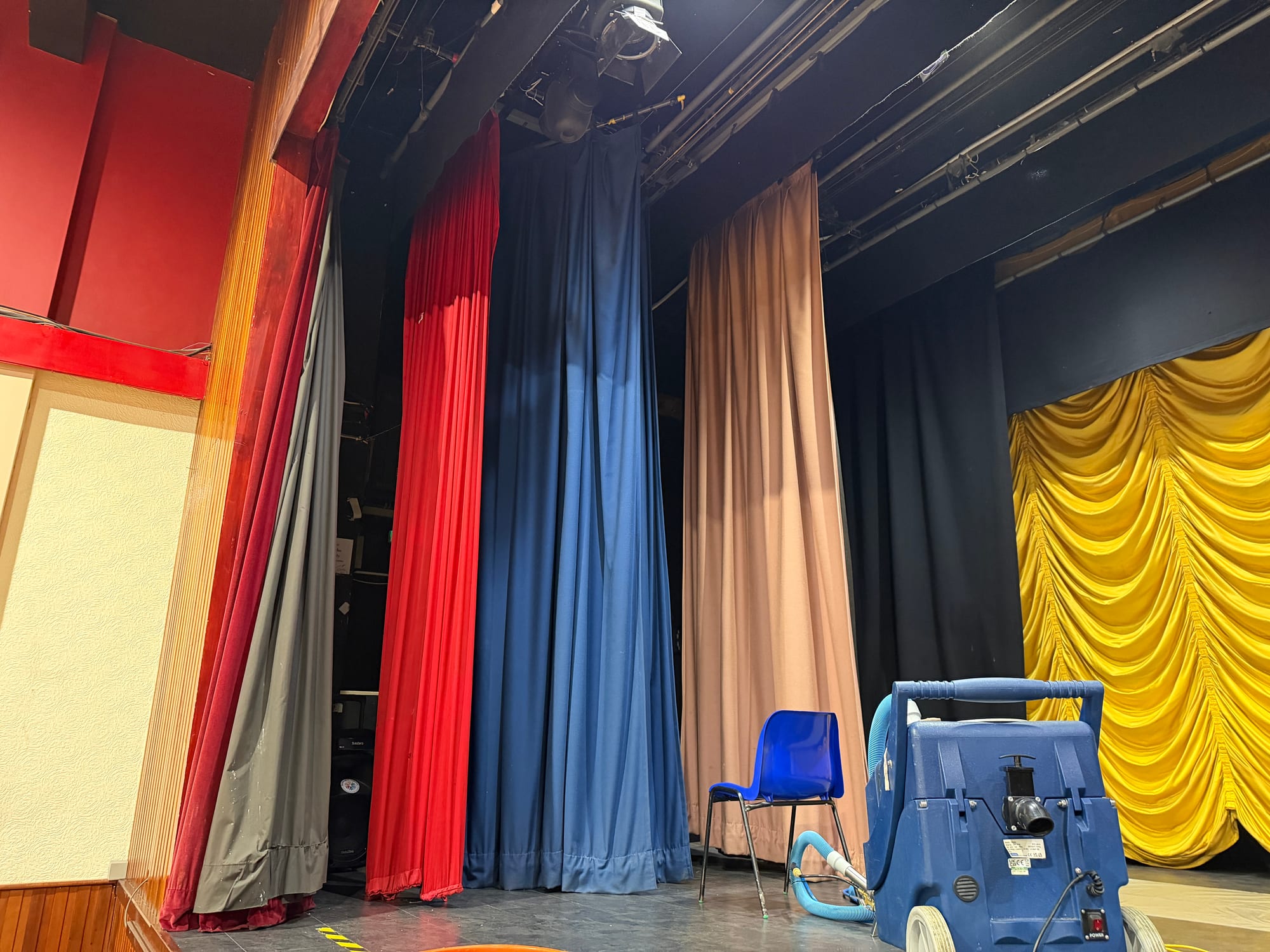 Colourful full-height theatre curtains with professional cleaning equipment on stage