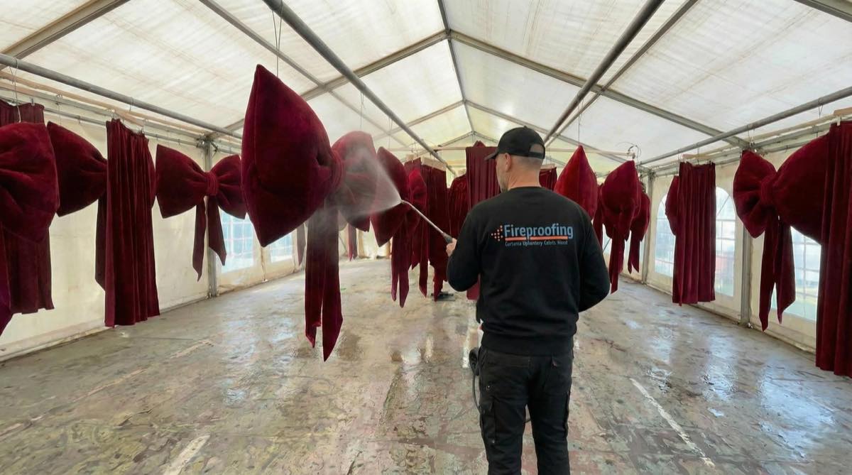 Fire Proofing Ltd technician applying fire retardant to large red scenic fabric